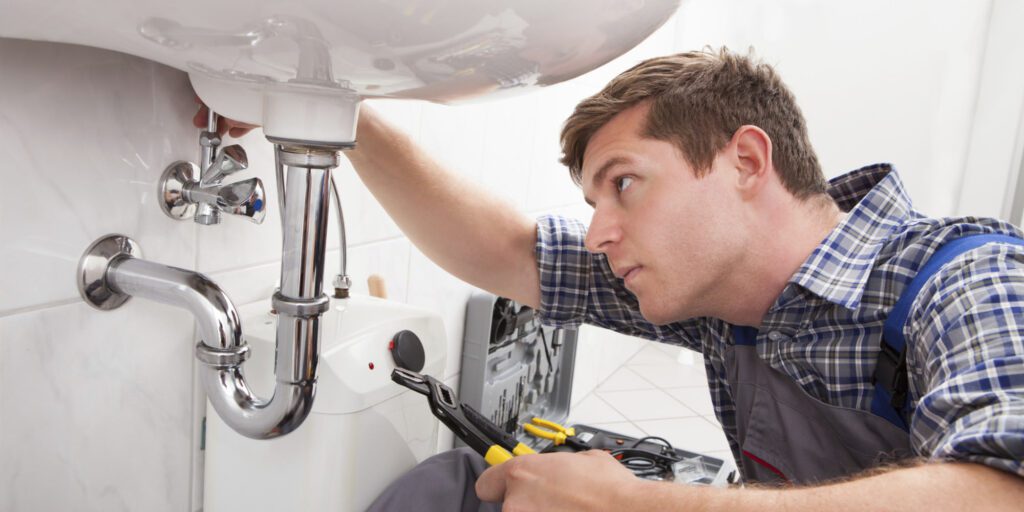 Young plumber fixing a sink in bathroom